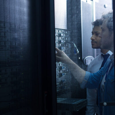 Modern data center. Handsome serious male technician standing near his colleague and looking at the network server while pressing a button