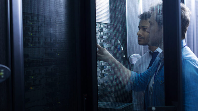 Modern data center. Handsome serious male technician standing near his colleague and looking at the network server while pressing a button