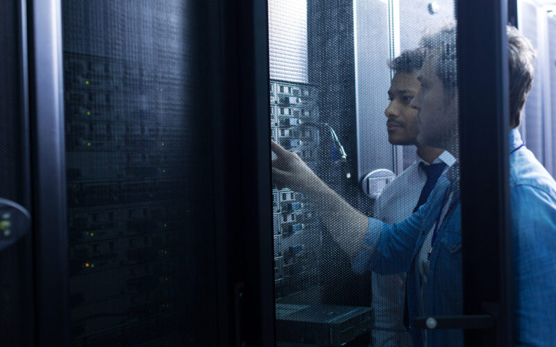 Modern data center. Handsome serious male technician standing near his colleague and looking at the network server while pressing a button