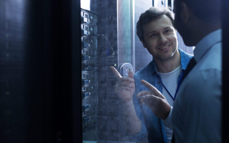 Pleasant cooperation. Nice positive delighted man smiling and looking at his colleague while pointing at USB cables