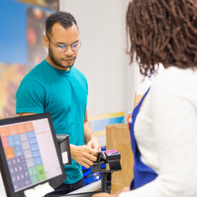 Focused young man paying bill in store. Back view of cashier standing at workplace. Shopping concept