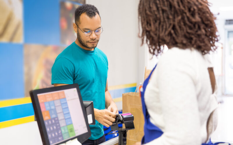 Focused young man paying bill in store. Back view of cashier standing at workplace. Shopping concept