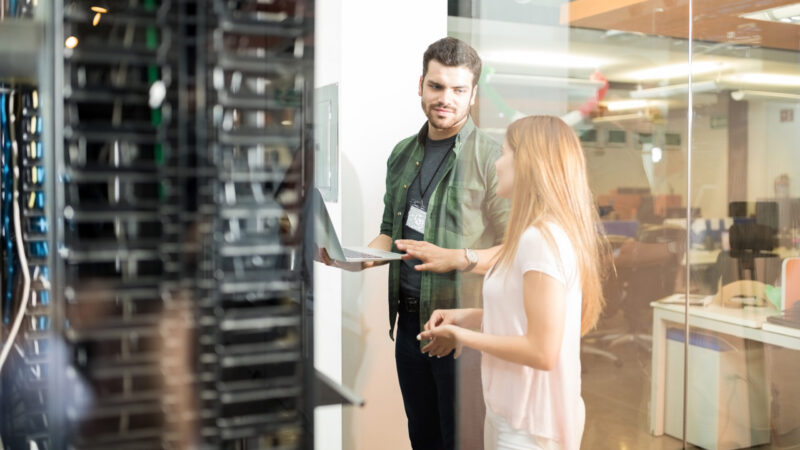 Two business people standing in server room with laptop and discussing