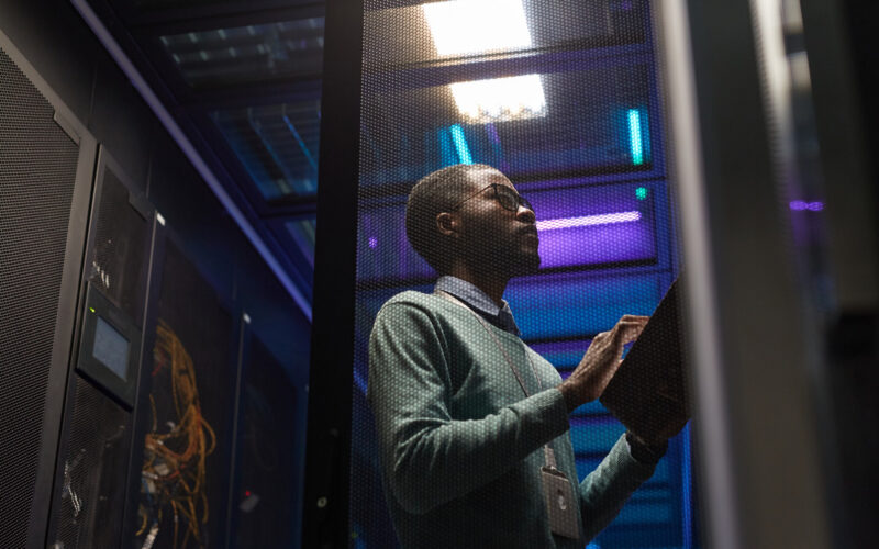 portrait-contre-plongee-ingenieur-donnees-afro-americain-travaillant-superordinateur-dans-salle-serveurs-eclairee-par-lumiere-bleue-espace-copie (1)